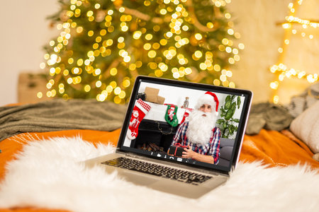 Santa Claus at laptop computer in his workshop having video call, Xmas present. Gift-giving, self-isolation, virtual Christmas celebration at home conceptの写真素材