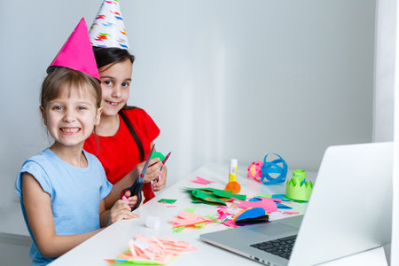 Kids online birthday party. Little girls in dresses, hat celebrate holiday with friends. Conference,video call in laptop, computer. Quarantine, coronavirus pandemic covid-19.の写真素材