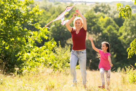 happy family mother and child run on meadow with a kite in the summer on the natureの写真素材