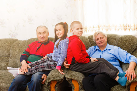 Happy young boy and girl with their laughing grandparents smiling at the camera as they pose together indoorsの写真素材