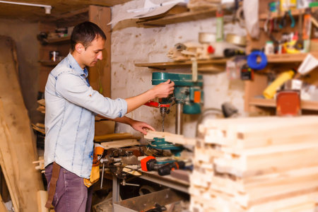 Satisfied cheerful joyful smiling woodmaster is standing near desktop in his workshop, workstation