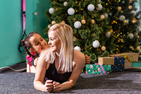 mother and daughter doing fitness near the christmas tree at gym. New Year. Christmas, holidays, fitness, and gym concept.の写真素材