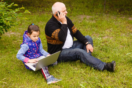 Smile attractive stylish grandfather using smartphone, granddaughter using laptop. using internet...