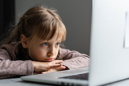 Bored little girl with laptop at home. Cute child doing homework on computer. Modern online education, communication and technology concept, copy spaceの写真素材
