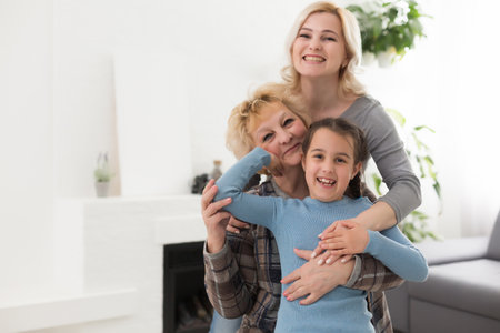 Portrait of three generations of women look at camera posing for family picture, cute little girl hug mom and granny enjoy time at home, smiling mother, daughter and grandmother spend weekend togetherの写真素材