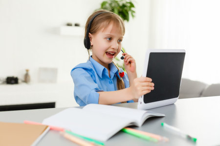 Cute little girl is sitting at table with her laptop and studying online