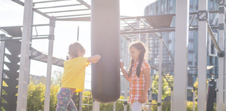 Two cute little girls having fun on a playground outdoors in summer. Sport activities for kids.