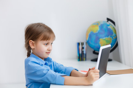Smart little schoolgirl with digital tablet in a classroom. Child in an elementary school. Education and learning for kids.の写真素材