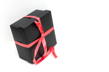 Black gift box with red satin ribbon and bow, over white background.