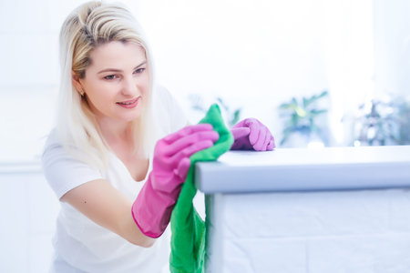 Cleanness is in trend. Pretty smiling woman wiping table with cloth and special means of washing