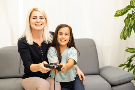 good relationship cute little girl with young mother using joystick playing video game sitting...