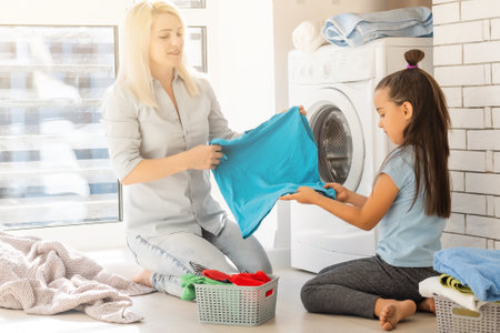 Happy housewife and her daughter with linen near washing machineの写真素材