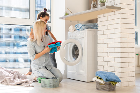 family mother and child girl little helper in laundry room near washing machine and dirty clothesの写真素材