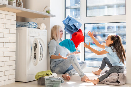 Happy housewife and her daughter with linen near washing machineの写真素材