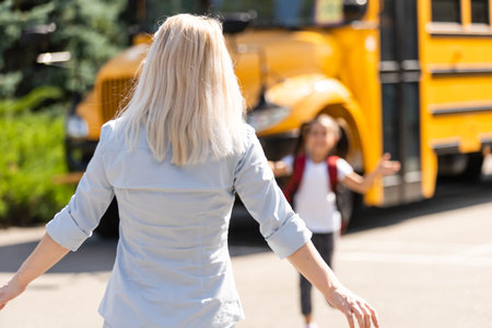 Kids student running into mothers hands to hug her after back to school near the school bus