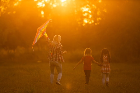 happy family mother and children run on meadow with a kite in the summer on the natureの写真素材