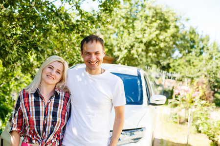 New car. Young adult joyful man and woman standing with hands up near a new car, happyの写真素材