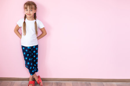 Beautiful little blonde girl with long hair in white T-shirt smiling on a pink backgroundの写真素材