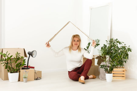 Happy young woman sitting on floor near moving boxes. Young woman moving to new home. Woman looking...