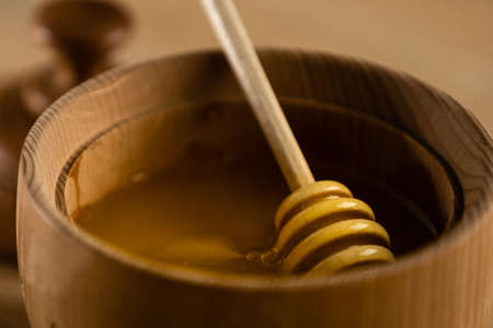Honey dripping from honey dipper in wooden bowl. Close-up. Healthy organic. Thick honey dipping from the wooden honey spoon, closeupの写真素材