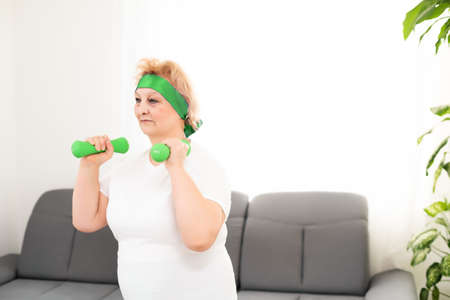 Closeup portrait of active senior woman doing dumbbell exercises at home, smiling.の写真素材
