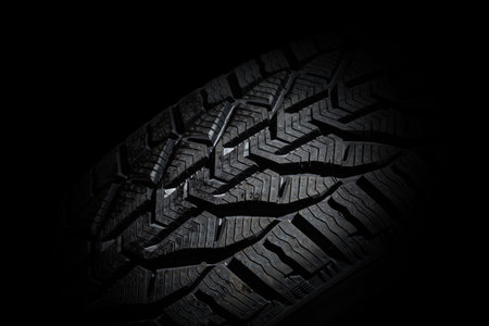 Closeup car tire isolated on black background. Wet with drops wheel against black