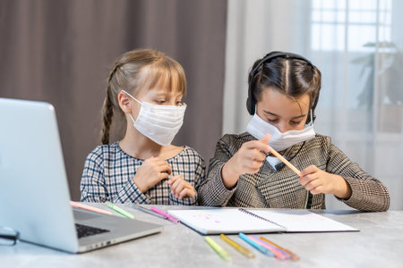 Young elementary school girls with face protective mask watching online education class. Coronavirus...