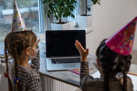 Young girls wearing a face mask during the Covid-19 or coronavirus pandemic on birthday sitting at a tableの写真素材