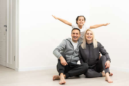 happy family father mother and children sitting on the floor in an empty white wallの写真素材