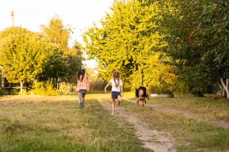 two little girls with dog running on the roadの写真素材