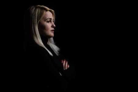 Closeup portrait of young female in black pullover with folded hands, over dark studio background.の写真素材