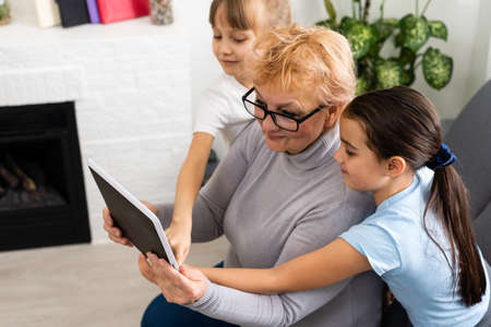 grandmother and two granddaughters use a tablet at homeの写真素材