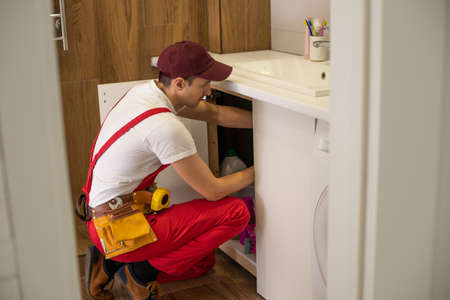 Worker installing doors on the closet. Furniture repair and assembly concept. Young man assembling bathroom furniture. Hands close up. Carpenter working with screwdriverの写真素材