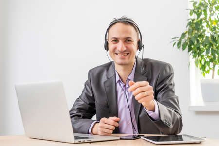 Man working in the office from dawn to dusk. Communication via the Internet. Young businessman using tablet laptop and headphones phone connecting wi-fi. Sunset light. Negotiations on line.の写真素材