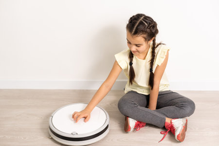 Little girl using robotic vacuum cleaner at homeの写真素材