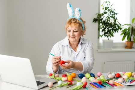 Beautiful senior woman with easter eggs and easter breads on the table at homeの写真素材
