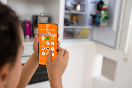 little girl holds a smartphone and controls the refrigerator, smart homeの写真素材