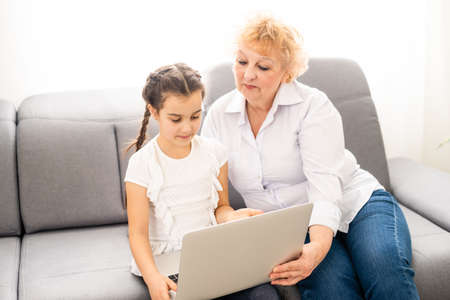 modern grandmother teaching grandchild how to use laptop computer at homeの写真素材