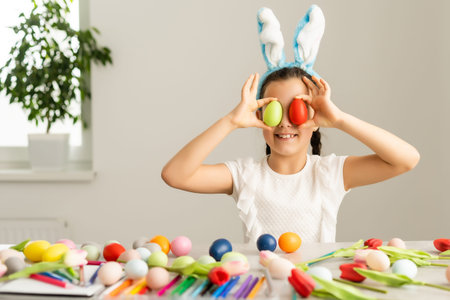 Easter holiday. Cute little girl in a protective medical mask with bunny ears with Easter eggs and...