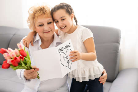 Little beautiful granddaughter gives her grandmother a bouquet of pink tulips. The concept of family, respect, generation, mother, upbringingの写真素材