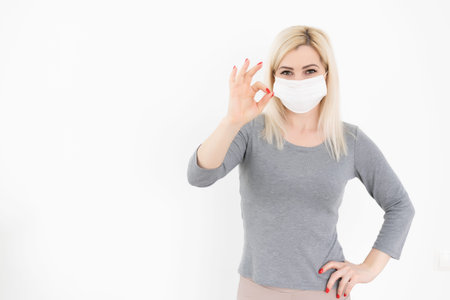 Young woman wearing medical face mask. Woman Wearing Protective Mask and Showing OK sign. Woman...