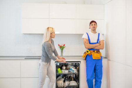 Young Woman Looking At Male Technician Checking Dishwasher In Kitchen