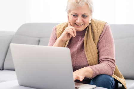 Elderly woman making video call on laptop, waving at screen, chatting with children, free spaceの写真素材