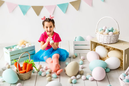 Getting ready to Easter. Lovely little girl holding an Easter egg and smiling with decoration in the backgroundの写真素材