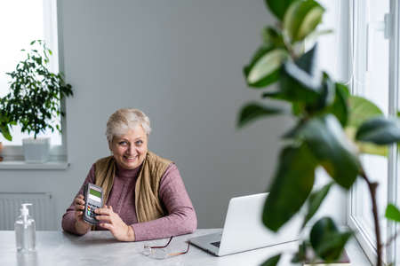 elderly woman sitting with laptop and bank terminalの写真素材