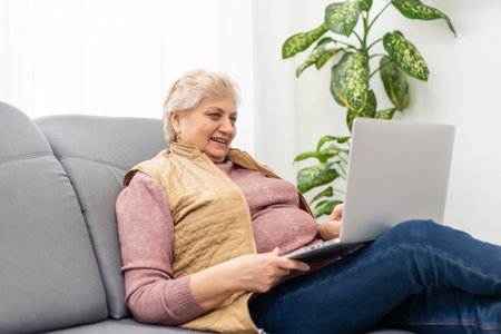 Elderly woman making video call on laptop, waving at screen, chatting with children, free spaceの写真素材