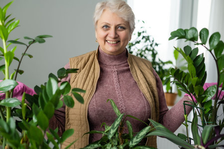Senior Woman With Green Plants and Flowers at home. Woman Caring for House Plant. Woman Taking Care of Plants at Her Home Portrait of Elderly Woman Gardening at Home. Retired Female Care for Her Plantの写真素材