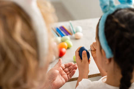 Elderly woman pains Easter egg yellow colour. Family preparing for Easter. Close-up hands with eggの写真素材