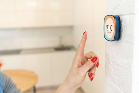 Smart home digital thermostat touch screen woman touching touchscreen to adjust temperature of heating in living room wallの写真素材