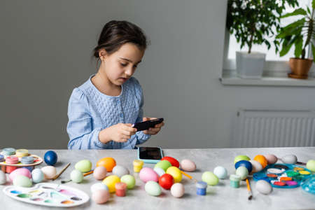 little girl takes pictures of painted eggs and paintsの写真素材